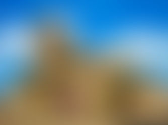 Historic cathedral with statues on a sunny day, against a blue sky with white clouds. Purple banners adorn the path, creating a serene scene.