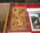 Vintage book titled "Noli Me Tangere" by J. Rizal displayed in a glass case, with decorative motifs and art print on the side.