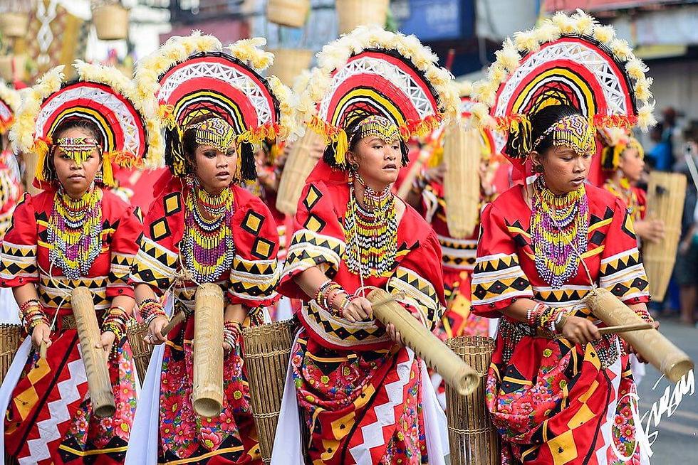Traditional Manobo dress Kaamulan Festival, Bukidnon, four people in vibrant red traditional attire perform in a street parade, wearing decorative headdresses and holding bamboo instruments.