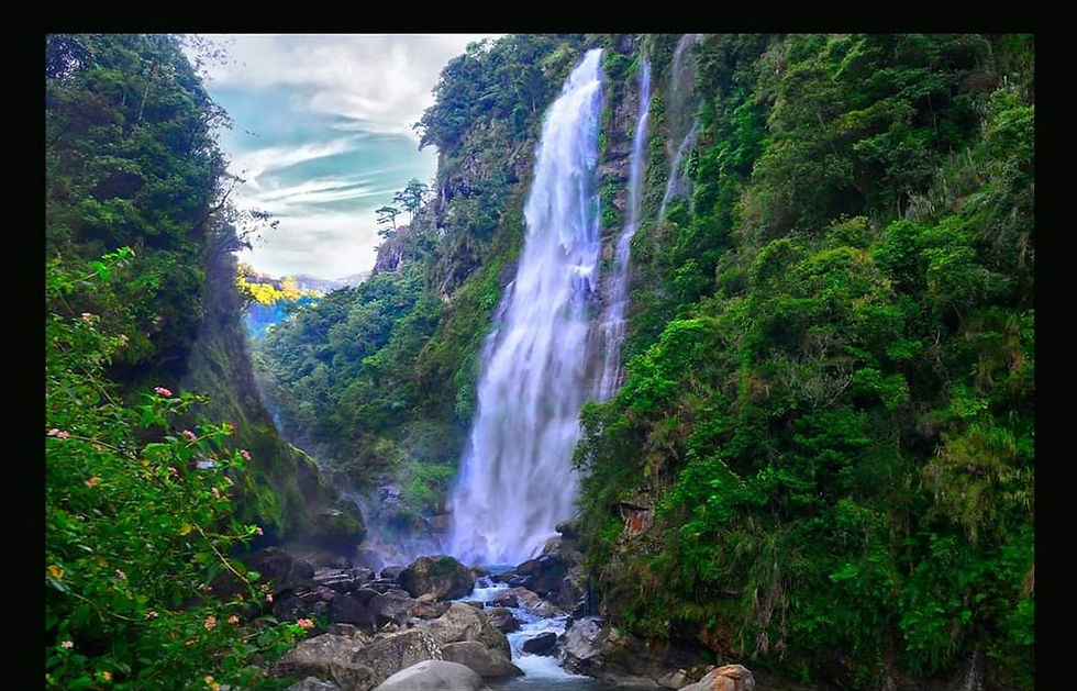 Bomod-ok Falls, waterfall cascading down a lush, green mountainside, surrounded by dense foliage and rocks under a partly cloudy sky, creating a serene atmosphere.