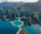 Aerial view of lush green mountains and turquoise lagoons with coral reefs. A small boat floats on clear blue water. Peaceful scenery.