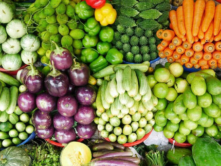 Colorful piles of fresh vegetables at a market: carrots, eggplants, limes, peppers, cucumbers and gourds arranged in baskets.