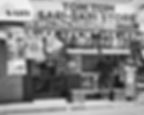 Man stands in front of Tom Tom Sari-Sari Store. Black and white image with text about LTE SIMs and promotions. Sunny day, street view.
