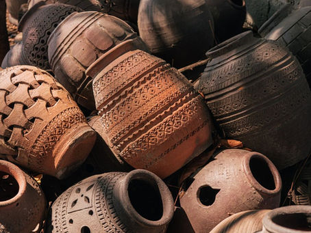 A cluster of intricately patterned clay pots in earthy tones, stacked together outdoors, showcasing a range of traditional designs under sunlight.