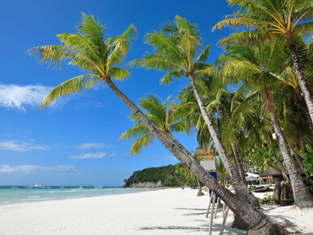 Boracay Island, palm trees lean over a pristine white sandy beach under a clear blue sky, with turquoise waters and distant sailboats in a tropical setting.