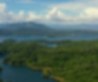 Aerial View of Pantabangan Lake, a lush green forest with blue lake and distant mountains under a partly cloudy sky, conveying a serene and natural landscape.