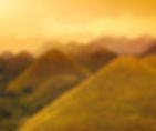 Chocolate Hills, rolling hills with brown grass under an orange sky. The scene is serene and bathed in warm, golden light, evoking tranquility.