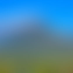 A lush green mountain with a flowing white cloud at its peak under a bright blue sky. A village with colorful rooftops lies below.