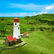 Lighthouse with red roof on green hills under a blue sky. Scenic landscape with sea in the background. Bright and peaceful setting.