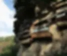 Hanging Coffins of Sagada, wooden coffins hang on a rocky cliff, some with painted names. Sunlight casts shadows, with green trees visible in the background.