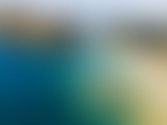 Aerial view of a tropical bay with lush green hills, clear turquoise water, and boats. Sandy beach and scattered buildings visible.