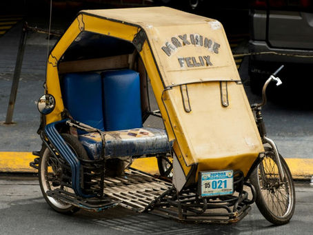 Yellow Pedicab tricycle with blue seats parked on a street. Text "MAXINNE FELIX" on canopy. Bright sunlight, urban setting. License plate visible.