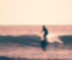 Looking at a silhouette of a surfer on the wave in an almost pink sunset.