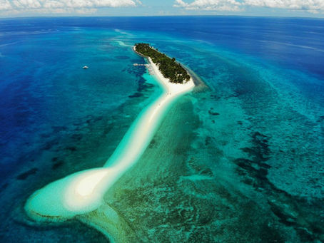 Kalanggaman Island an aerial view of a narrow, sandy island surrounded by turquoise ocean. Lush palm trees and a few boats line the coastline. Clear blue sky.