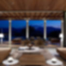 Amanzoe, a elegant open living room with beige sofas and modern decor, overlooking a serene evening landscape through large windows. Soft lighting sets a calming mood.