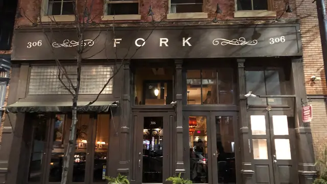 Nighttime street view of the historic brick facade and entrance to Fork restaurant at 306 Market Street in Philadelphia's Old City, featuring the prominent illuminated "FORK" signage, double doors, potted ferns, and warm interior lighting glowing from within.