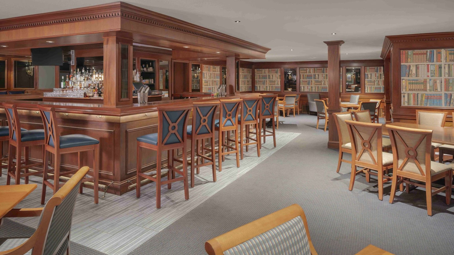 Elegant hotel bar with mahogany woodwork library shelves and bar seating at The Armory Lounge Portland Regency Hotel