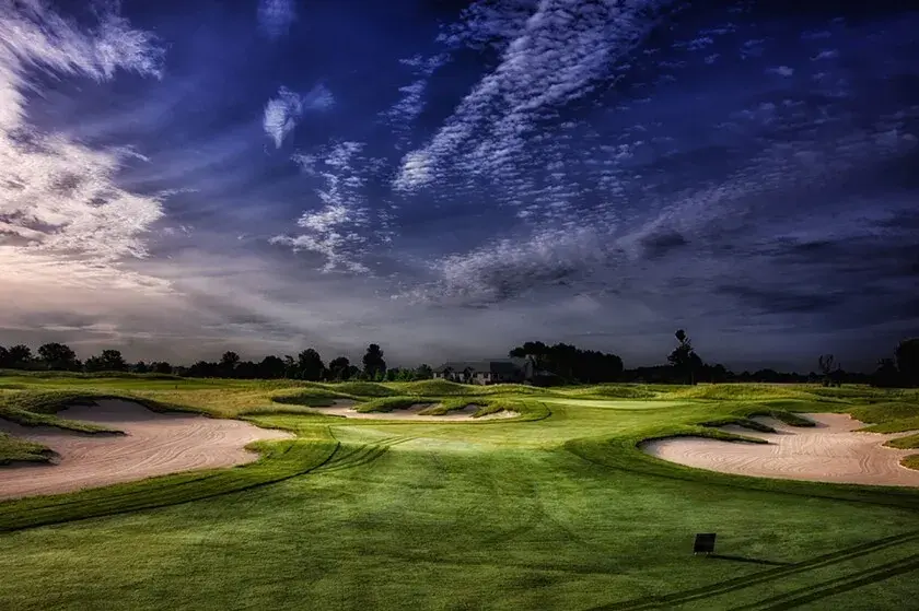 Breathtaking high-resolution photograph of Purgatory Golf Club showcasing multiple large, strategically placed sand bunkers surrounding pristine manicured rolling fairways and greens, with dramatic dark blue and purple storm clouds filling the sky in a cinematic twilight scene that highlights the course’s iconic links-style drama and natural beauty.