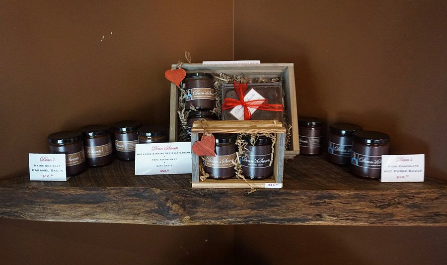 Rustic wooden display featuring gift crates, caramel sauce jars, and chocolate bars artfully arranged with red ribbon accents at Dean’s Sweets in Portland, Maine.