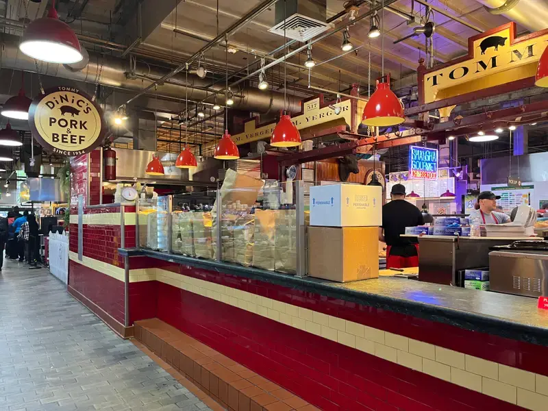 Wide view of DiNic's red-tiled counter and ordering area inside Reading Terminal Market with hanging red lights and signage.