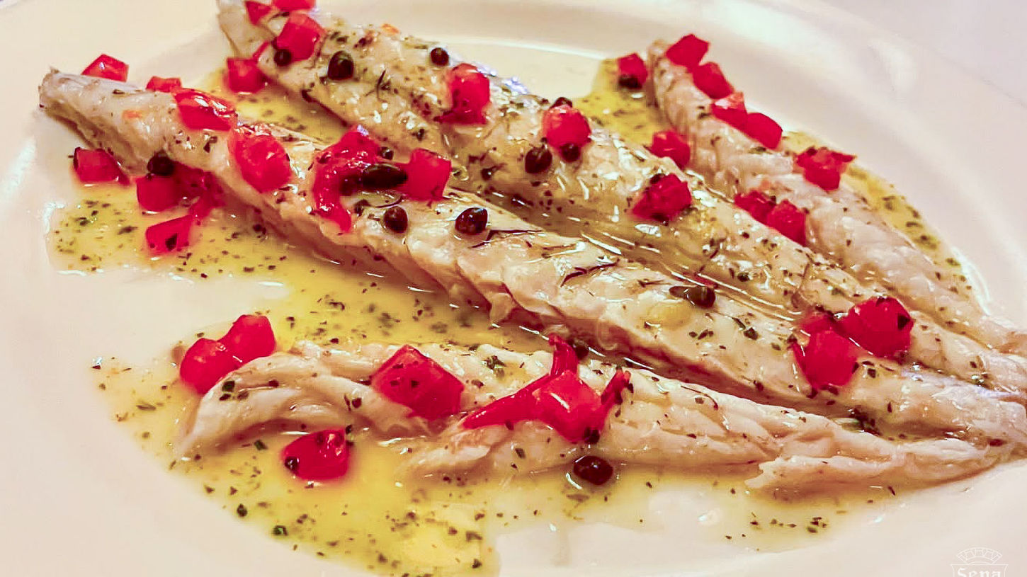 Plated white fish fillets with red pepper garnish, capers, and herb-infused sauce from the La Famiglia Ristorante menu.