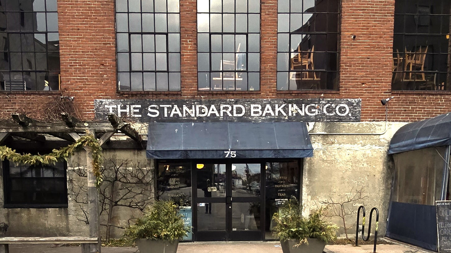 Charming red-brick exterior of Standard Baking Co. at 75 Commercial Street in Portland’s Old Port, featuring the iconic blue awning, large windows, and welcoming entrance with potted plants.