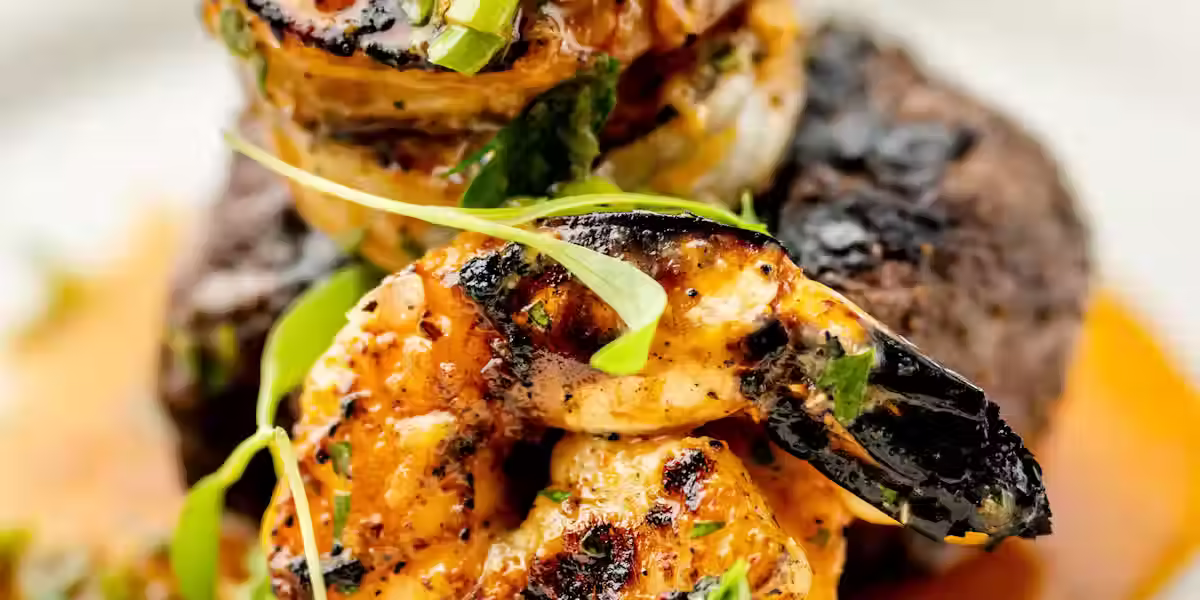 Close-up of a beautifully plated surf and turf entrée at Mr. Paul’s Supper Club featuring grilled shrimp, seared steak, vibrant herbs, and rich sauce on a white plate.