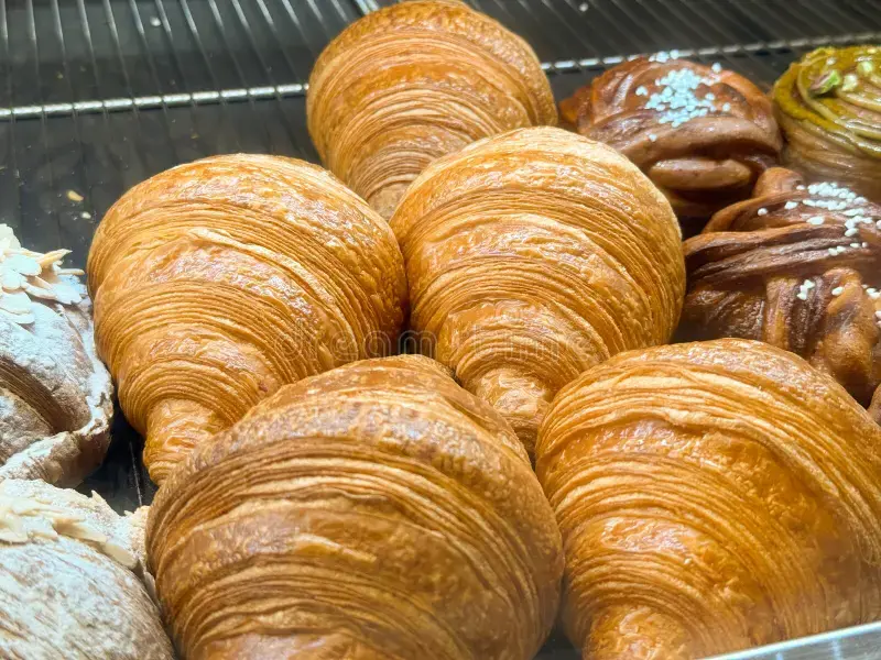 Detailed close-up of golden, flaky croissants and fresh muffins arranged on a wooden board at Patisserie 46, highlighting the perfect layers and artisanal texture.