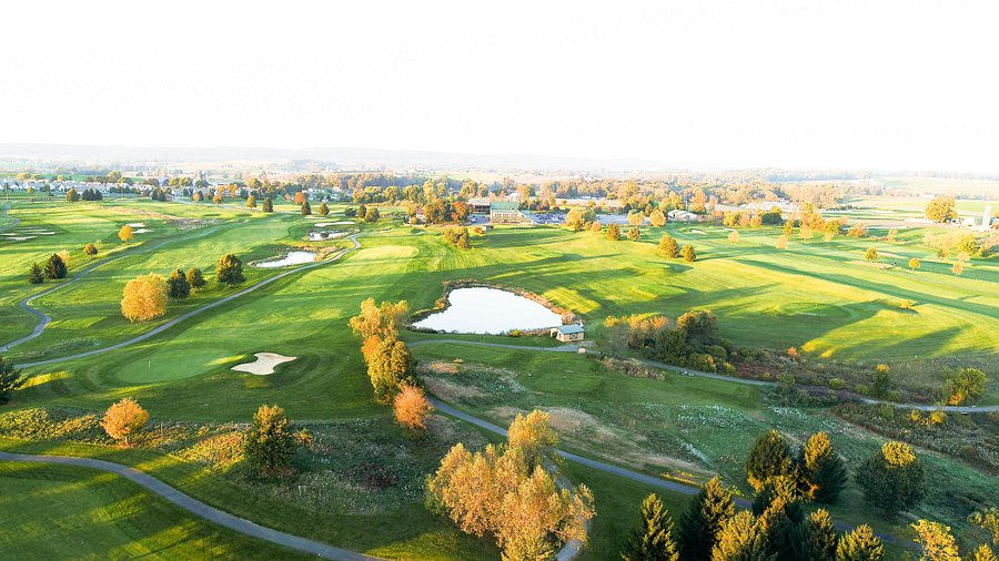 Stunning golden-hour aerial of Honeybrook Golf Club with pond, autumn trees, fairways, and distant views.