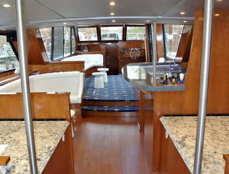Warmly lit interior cabin with rich wood finishes, granite countertops, blue star-patterned carpeting, plush white seating, and a full-service bar, showcasing the refined luxury of the private yacht.