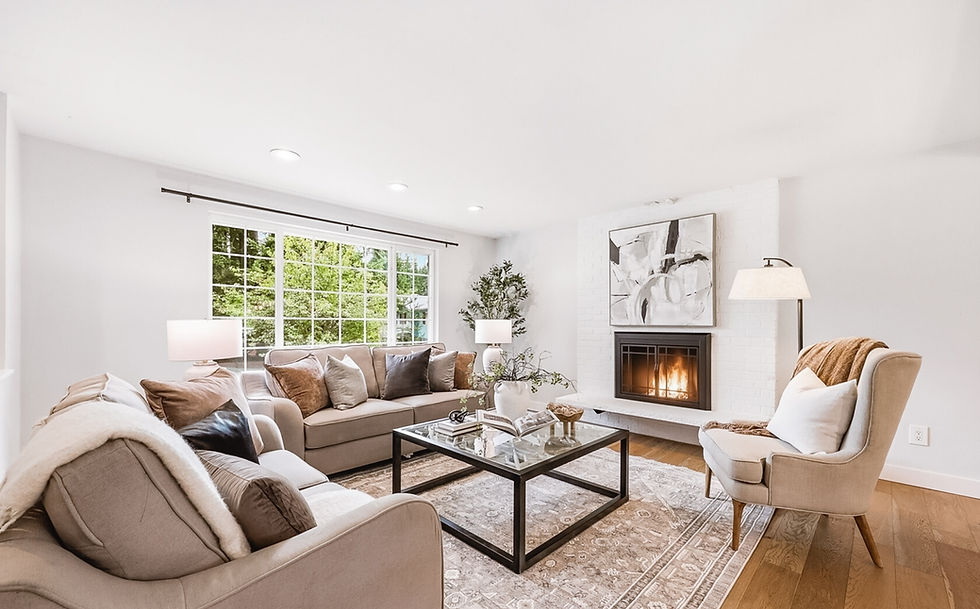 Bright neutral living room with beige sofas, fireplace, glass coffee table, large window, and cozy modern decor