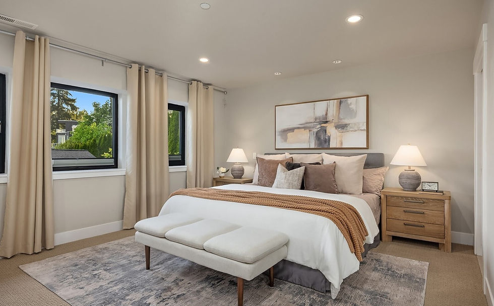 Cozy bedroom with a large bed, brown pillows, and an orange throw. Beige curtains, abstract art, and two lamps create a serene ambiance.