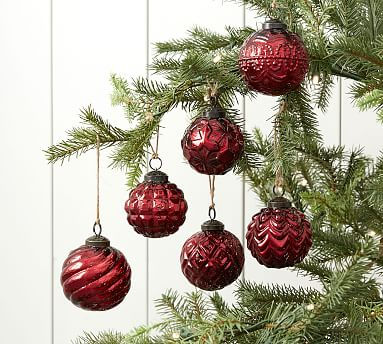 Red mercury glass ornaments shimmering as they hang gracefully on a lush green pine tree.