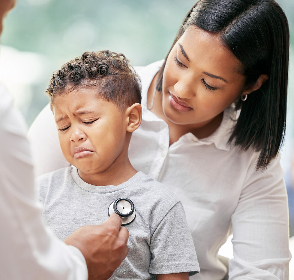 Photo of a young boy crying, sitting in his mother's lap while a pediatrician examines him.