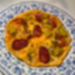 Spanish-style open omelette (tortilla vaga) topped with slices of chorizo, green peppers, and chopped chives, served on a blue and white floral plate
