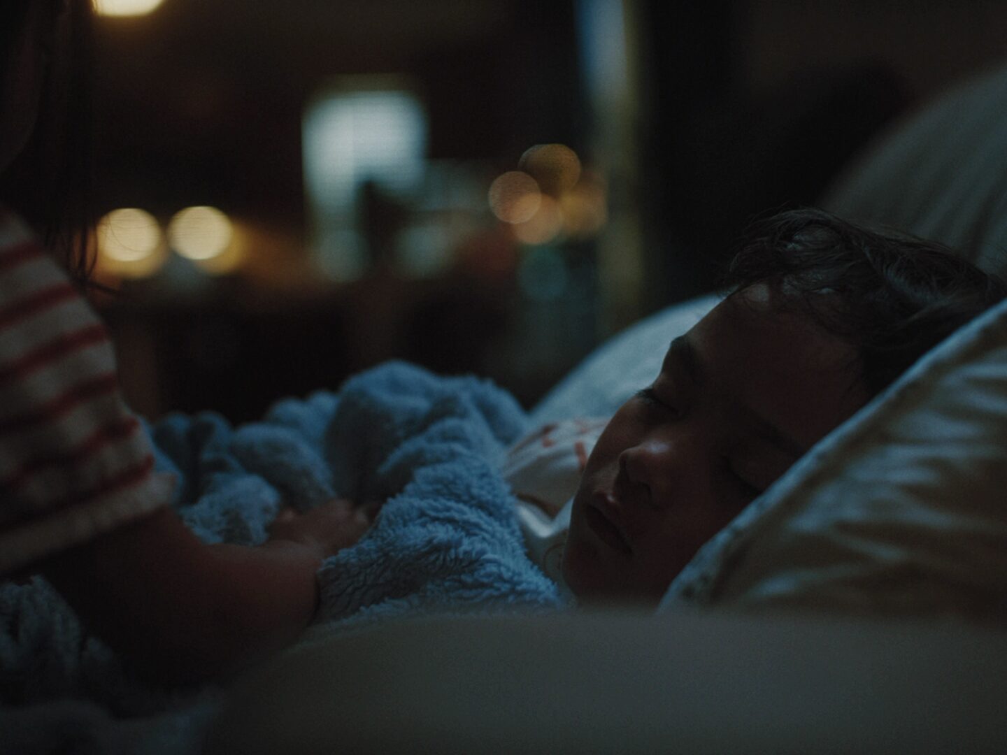 A mother tucks a sleeping child into bed at night