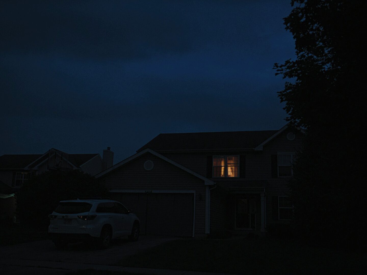 A suburban house at dusk with one window lit, from Anak