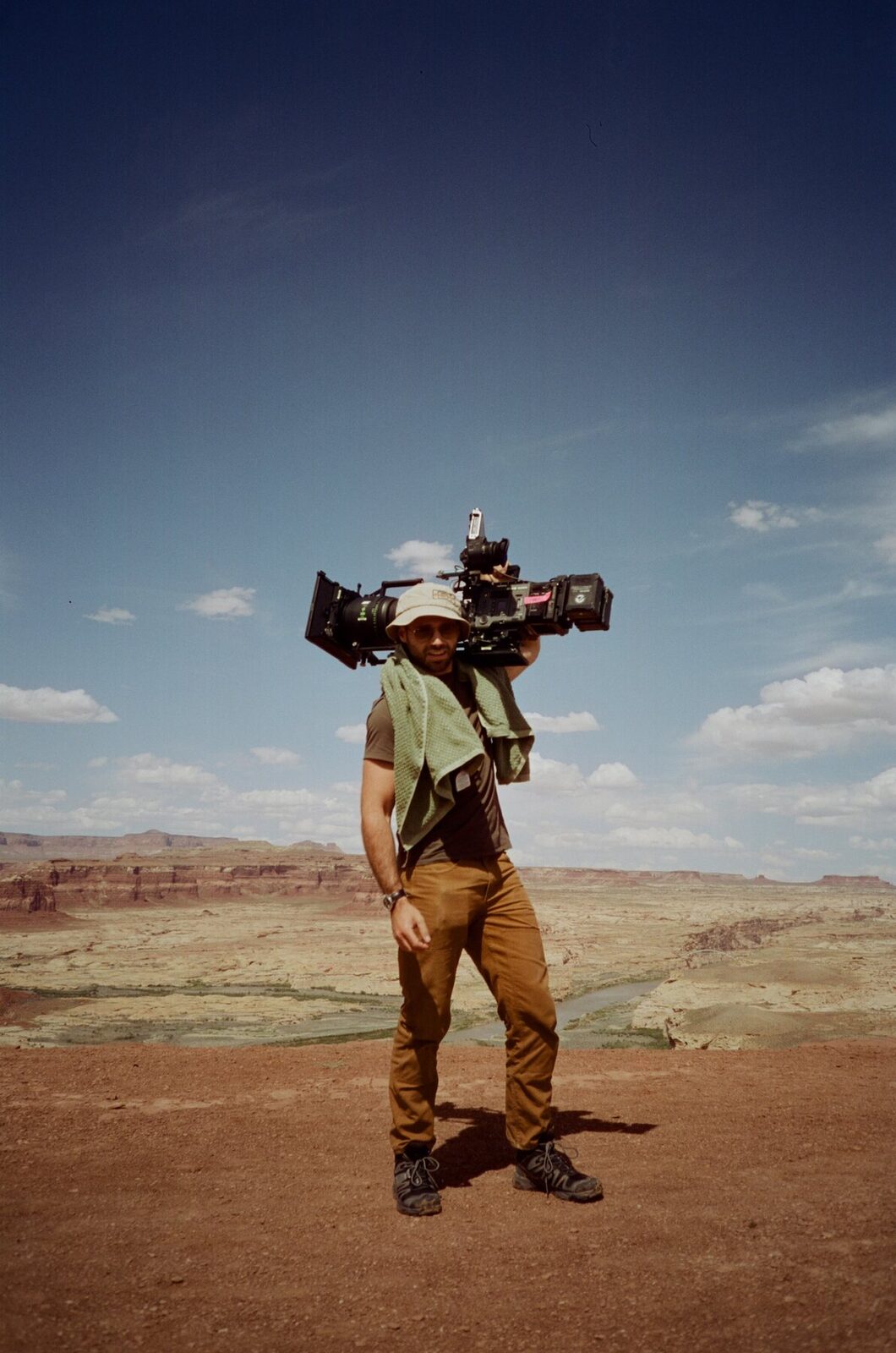 Elias carrying a camera on his shoulder in the desert
