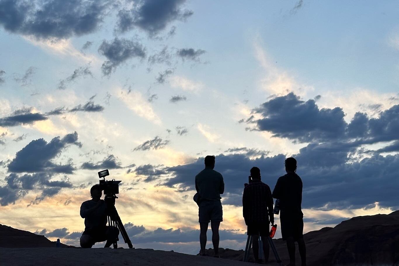Crew silhouetted against a sunset sky with a camera on a tripod