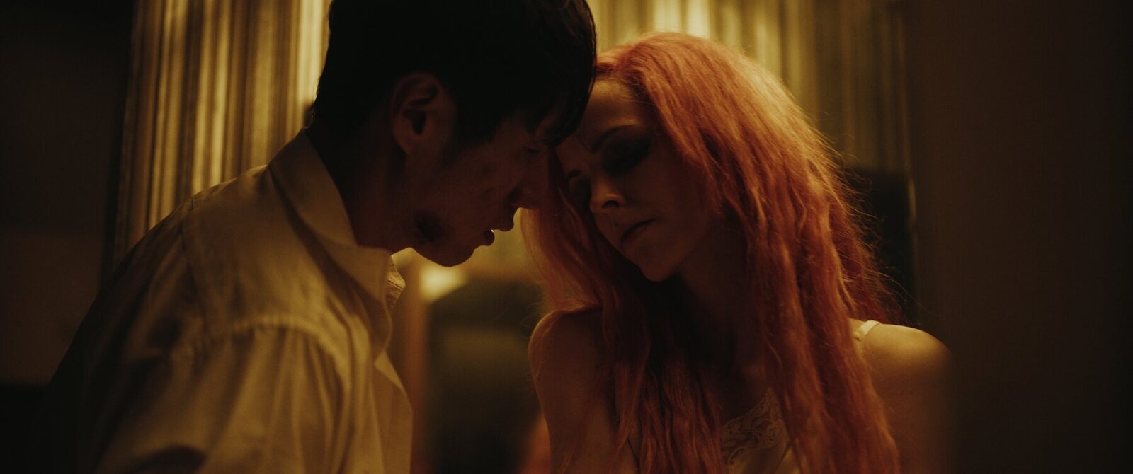 Two characters from Venus in Furs, foreheads touching, in warm amber light
