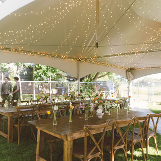 backyard tent wedding with string lights and wooden tables chairs bud vases