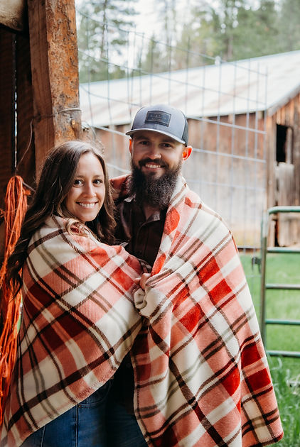Dylan and Lexie wrapped in a red plaid blanket outside a rustic barn, representing Hilltop Roofing's family roots