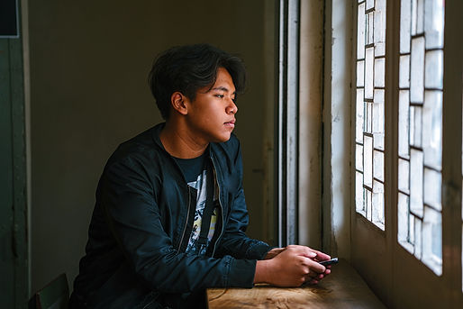 A college student looks down as he looks out a window.