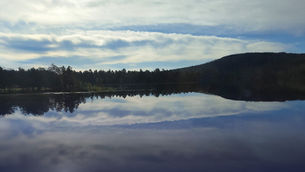 Silhouette of a forested ridge above a blue lake, the reflection of the sky and landscape in the water.