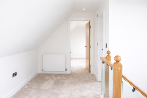 Loft landing with sloped ceiling, soft carpet, radiator, and wooden balustrade leading to adjoining rooms.