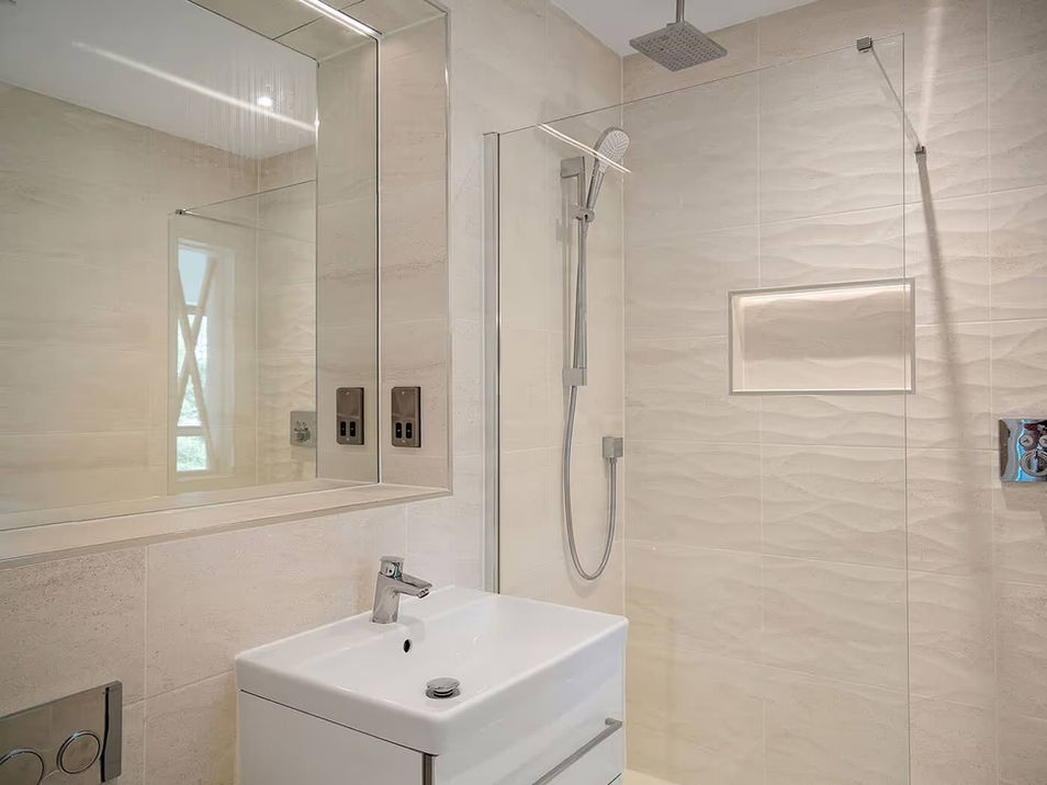 Modern bathroom with beige tiles, a glass-enclosed rainfall shower, and a rectangular white sink with a sleek faucet. A large mirrored cabinet adds elegance.