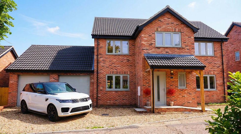 Red brick house with black roof and a white Range Rover parked on a gravel driveway. Blue sky and green shrub in foreground.