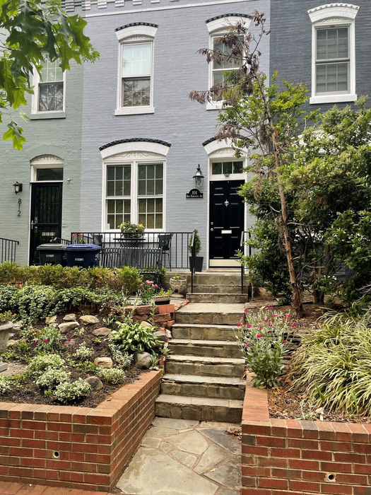 The sidewalk view shows a low red brick retaining wall and flagstone steps and patio. (D. Vogt, May 2022)
