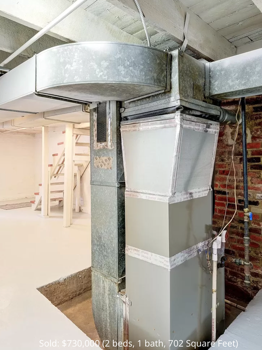 The lower level of the house with exposed brick walls and ceiling joists.
