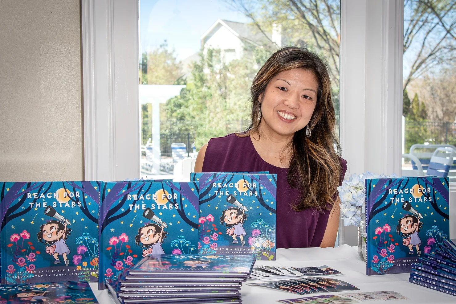 Michele Cho-Dorado behind a stack of Reach for the Stars books